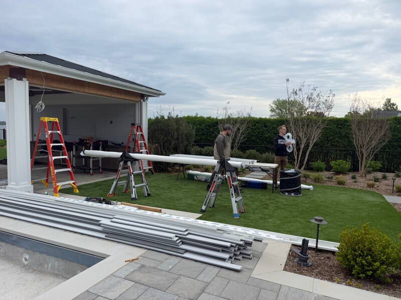 Smart Tek crew staging extruded aluminum screen tracks on the lawn beside the lakeside pavilion and pool