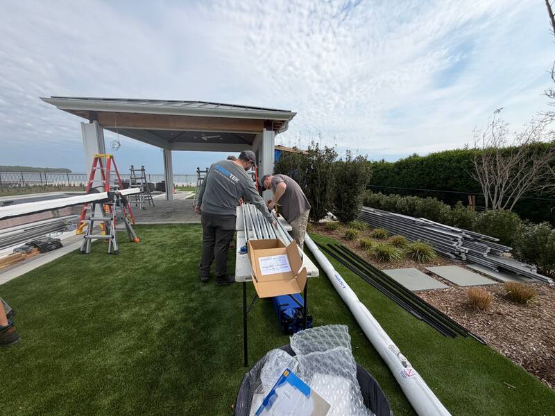 Two Smart Tek installers assembling aluminum screen track sections on a work table beside the waterfront pavilion