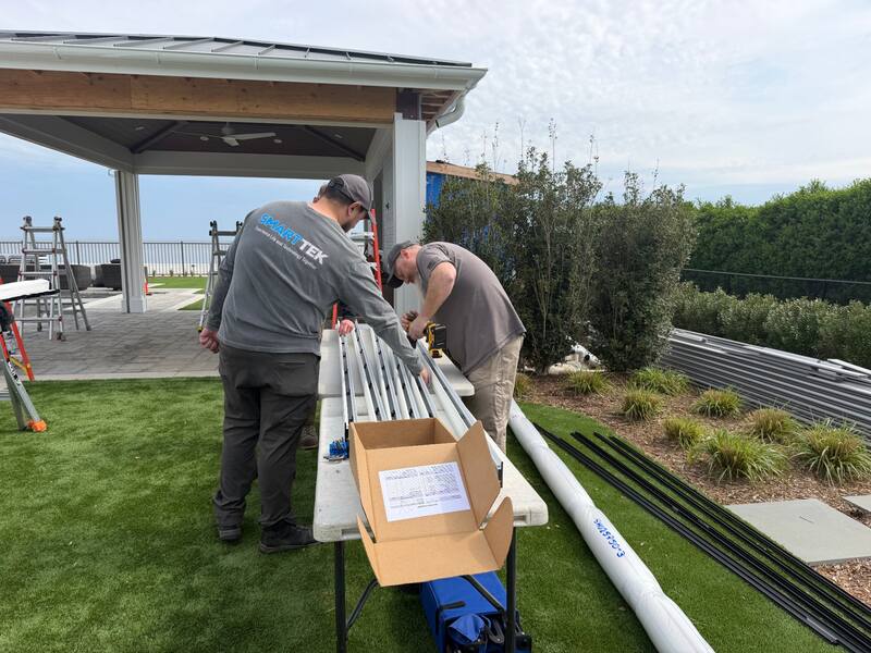 Smart Tek technicians in branded shirts drilling and prepping the motorized screen track assembly on site