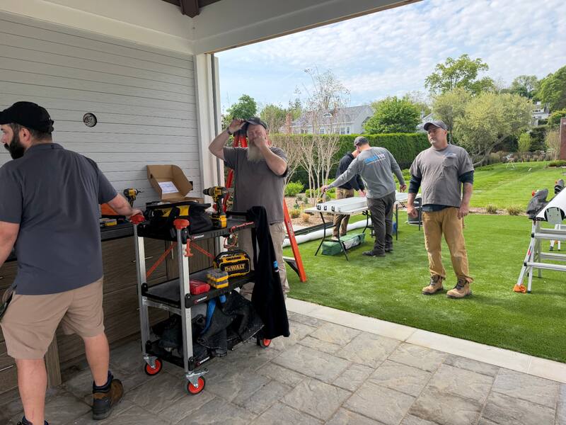 Smart Tek install team coordinating under the rear porch with tool cart, drills, and staged screen track components