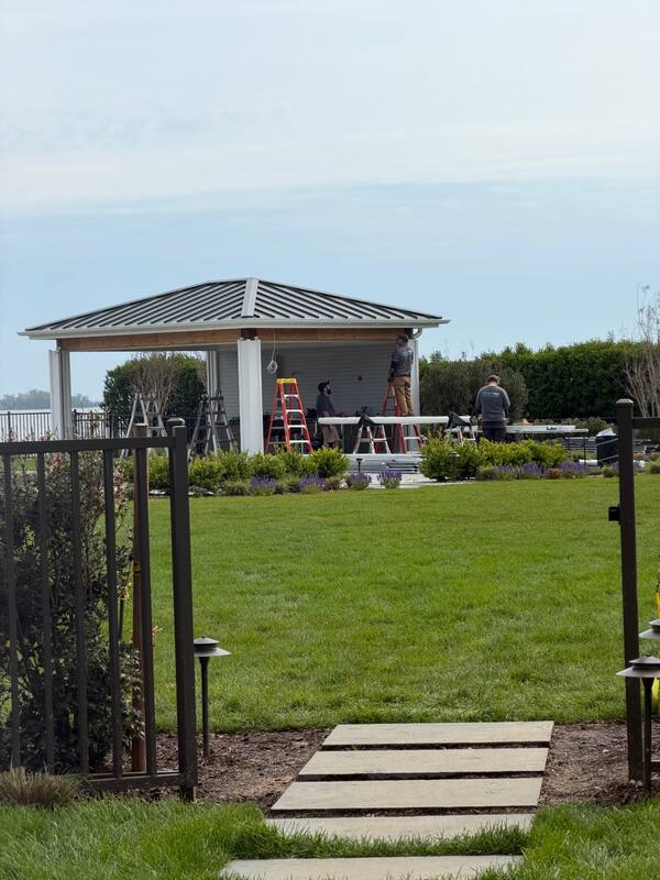 Waterfront pavilion with metal hip roof as Smart Tek technicians mount screen housings under the eaves
