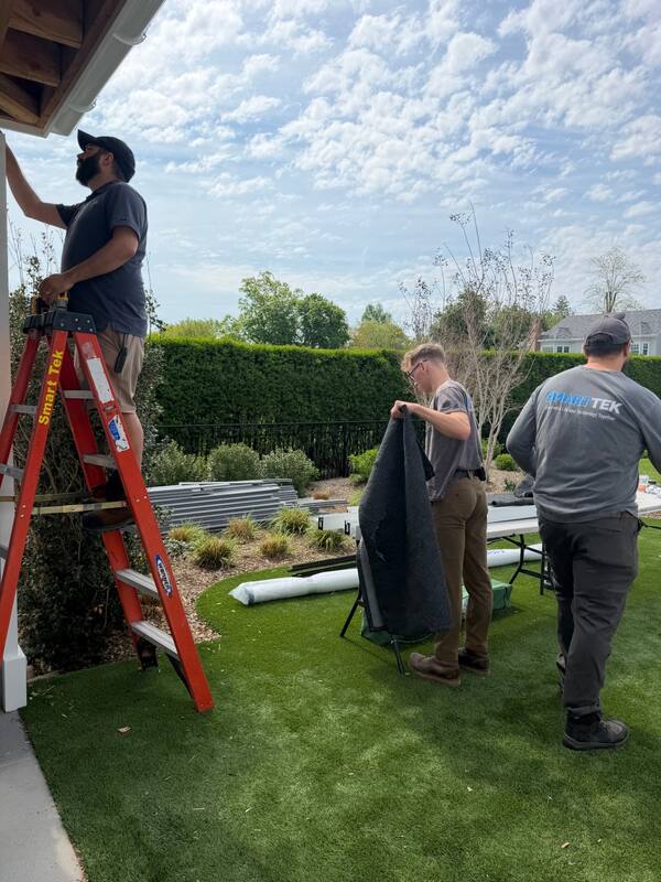 Smart Tek crew on ladders fastening screen housings to the porch ceiling while another tech unfolds the screen fabric