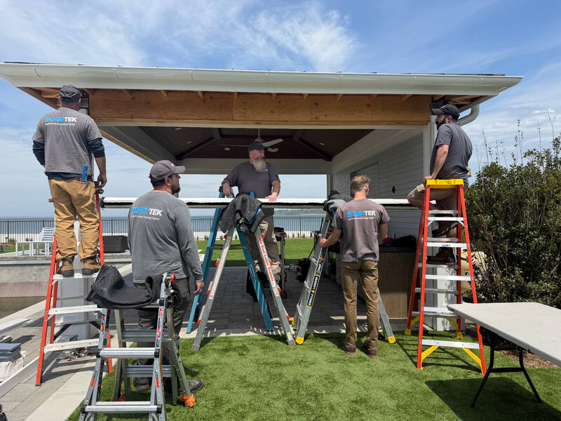 Smart Tek crew aligning a long motorized screen assembly across the front opening of the waterfront pavilion during final installation
