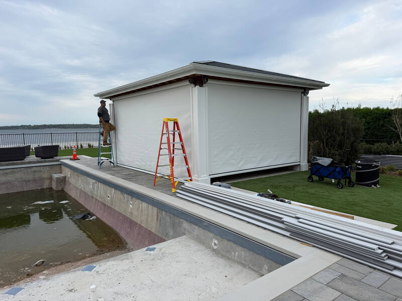 Completed waterfront pavilion with full-height motorized screens lowered on multiple sides for shade, wind, and insect protection