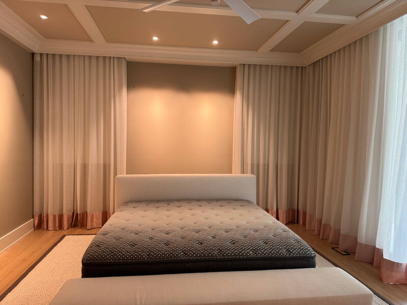 Upholstered bed beneath layered window treatments